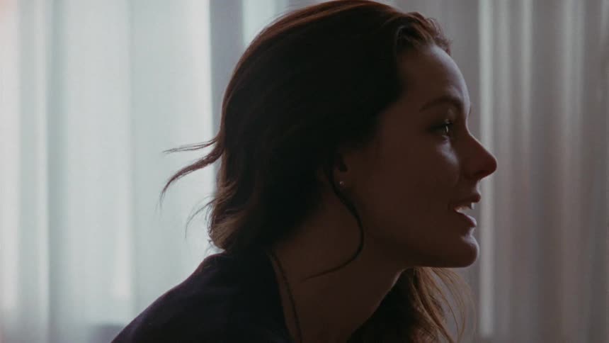 Long-haired brunette sitting indoors speaking to someone