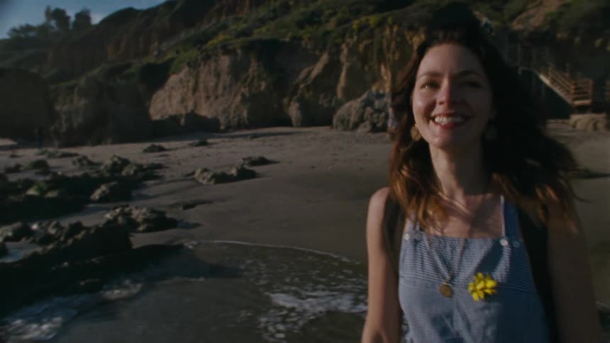A woman standing and laughing on a rocky beach