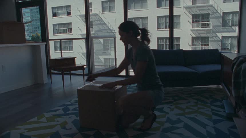 A woman cuts open a cardboard box in her living room