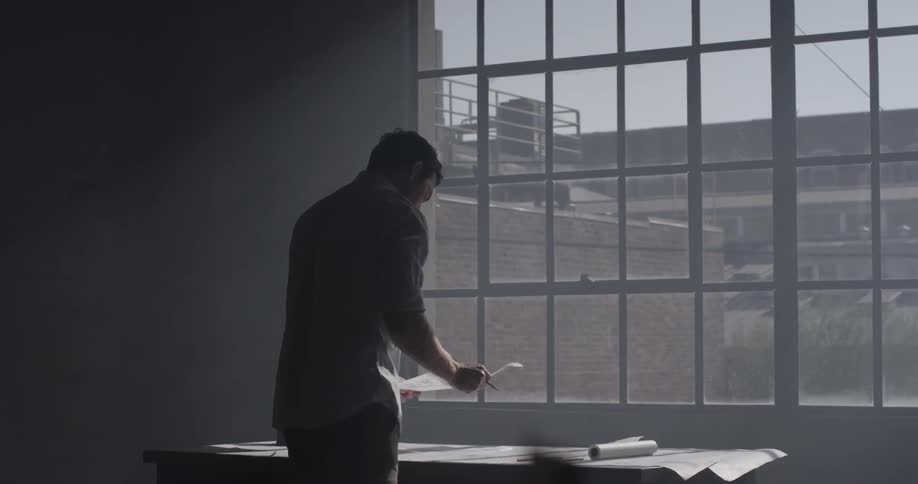 A man drawing on a piece of paper in front of a window