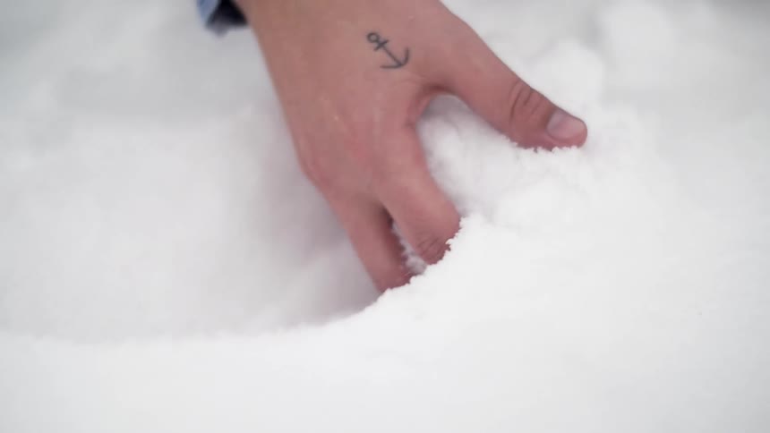 A hand with an anchor tattoo scoops up some snow