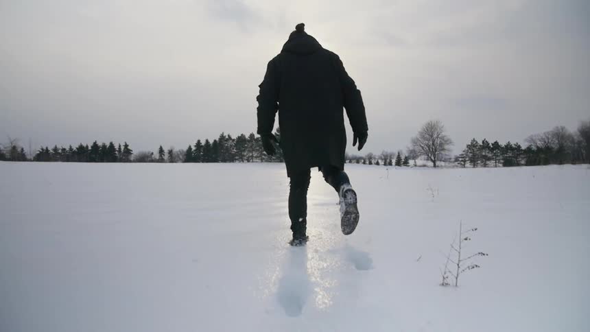 A man in a black coat and black pants trudges across the snow