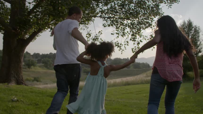 A man and woman swinging a girl by the arms outside