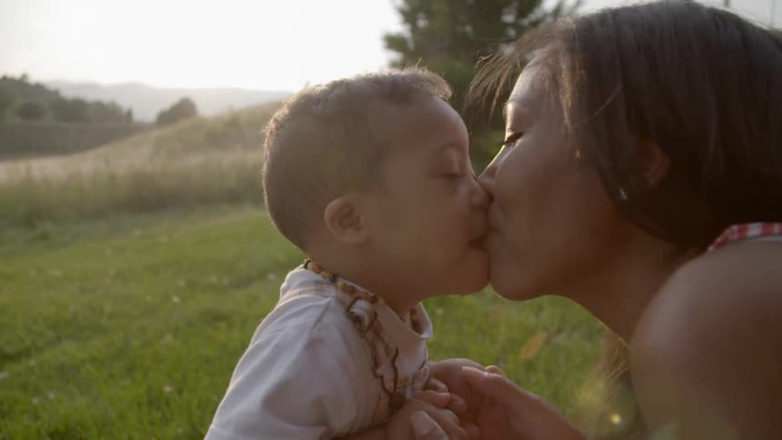 A woman kissing a toddler in a sunny field