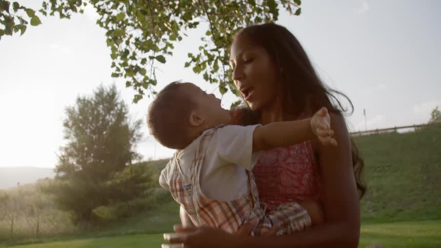 A woman standing under a tree holds a toddler