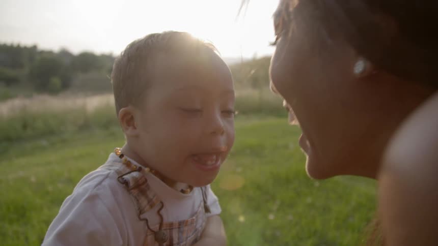 A woman kissing a toddler in a sunny field