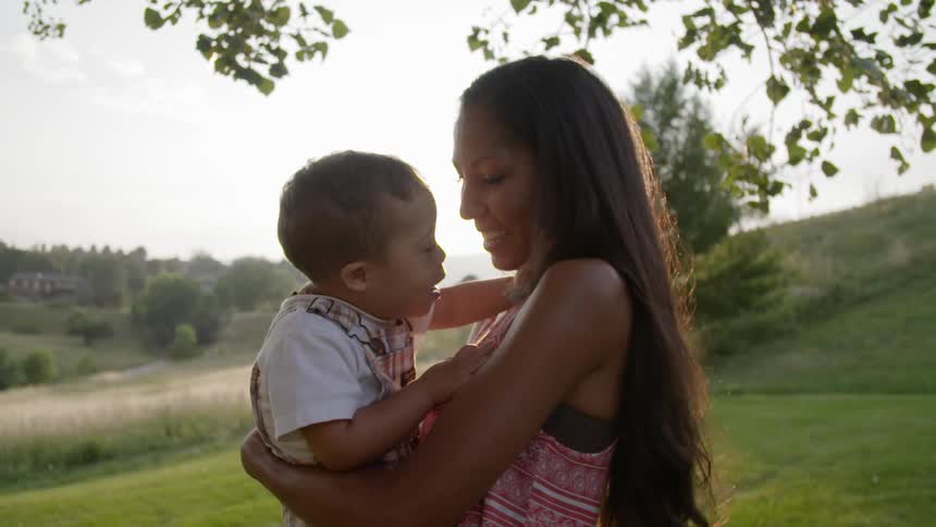 A woman holds her child in her arms as they laugh together on a sunny day