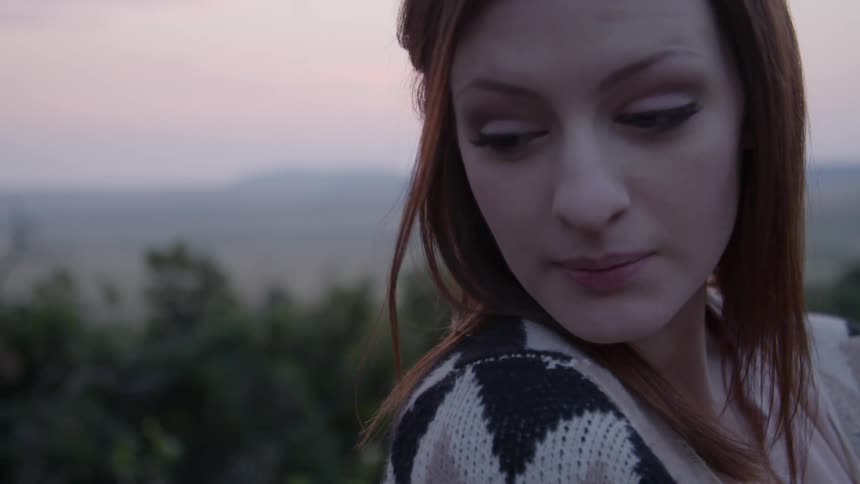 A woman stands atop a hill at sunset