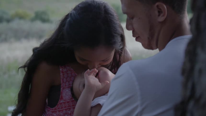 Hey man and woman stand in the field holding a child who looks upwards