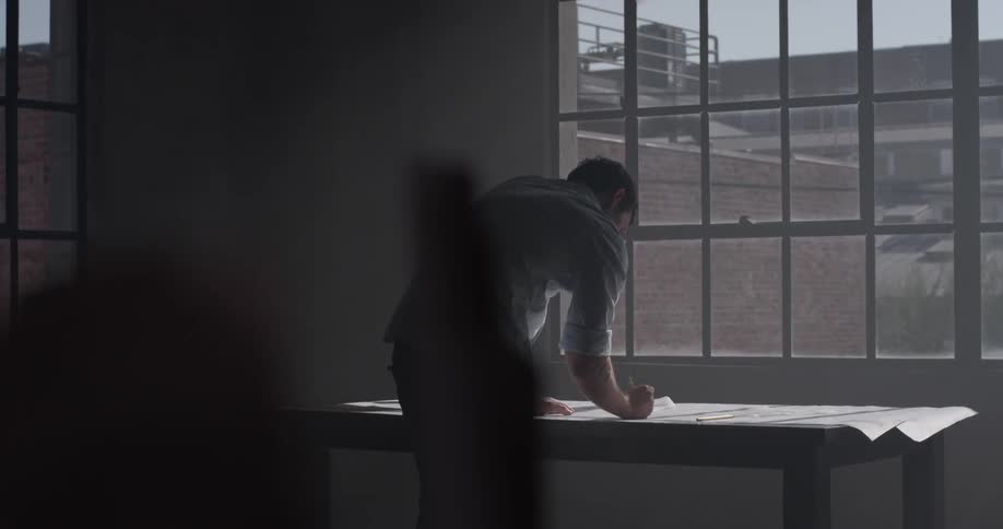 Man bends over and draws on a table in front of a window