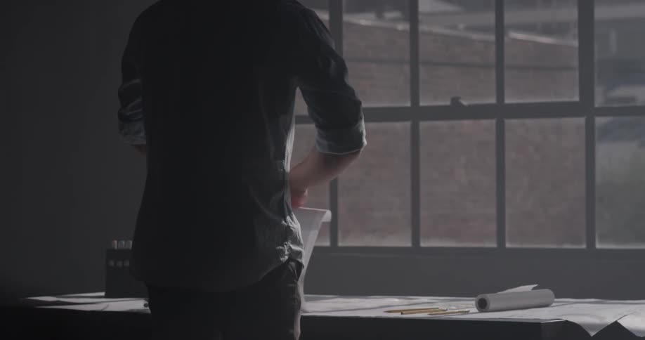 A man that is staring out a window while standing at a desk