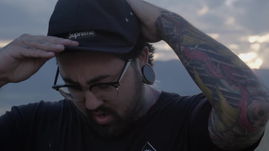 A man pushes back his hair then puts on a baseball cap