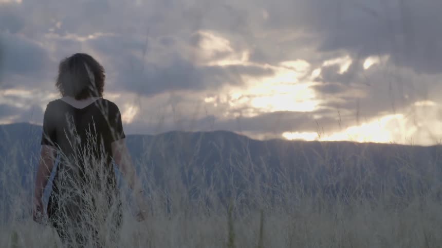 A woman walking through a grassy field at sunset
