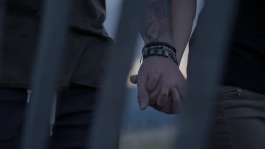 A couple holding hands as they walk alongside a fence on a cloudy day