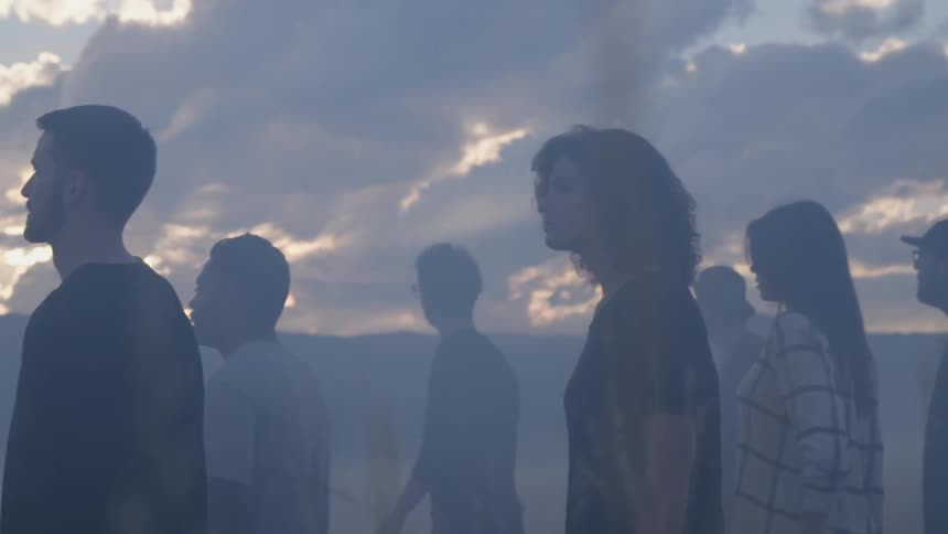 A group of people walking through a grassy field at sunset