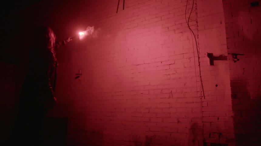 A woman uses a flare to light up a brick wall