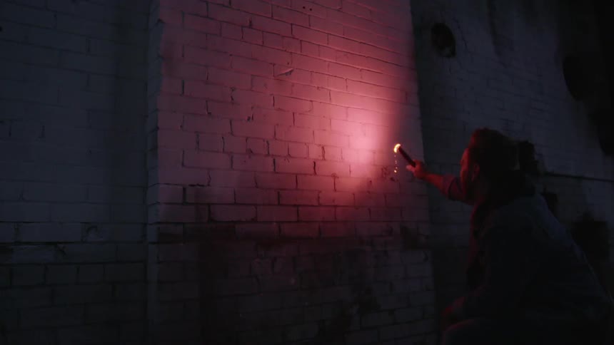 A man uses a flare to light up a brick wall