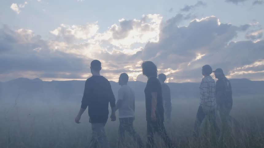 A large group of friends walks in an open field on a foggy morning
