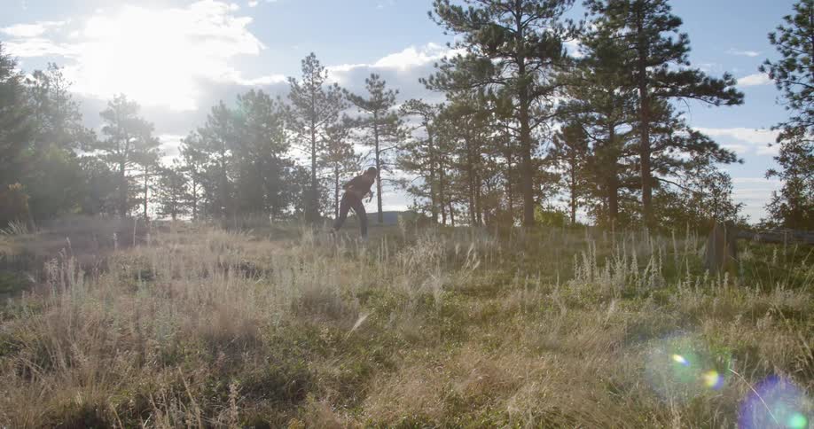 A woman standing in a natural setting shakes out her hands, crouches and then starts to run