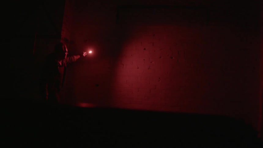 A man holding a flare near a wall and looking at the wall illuminated by the flare's light