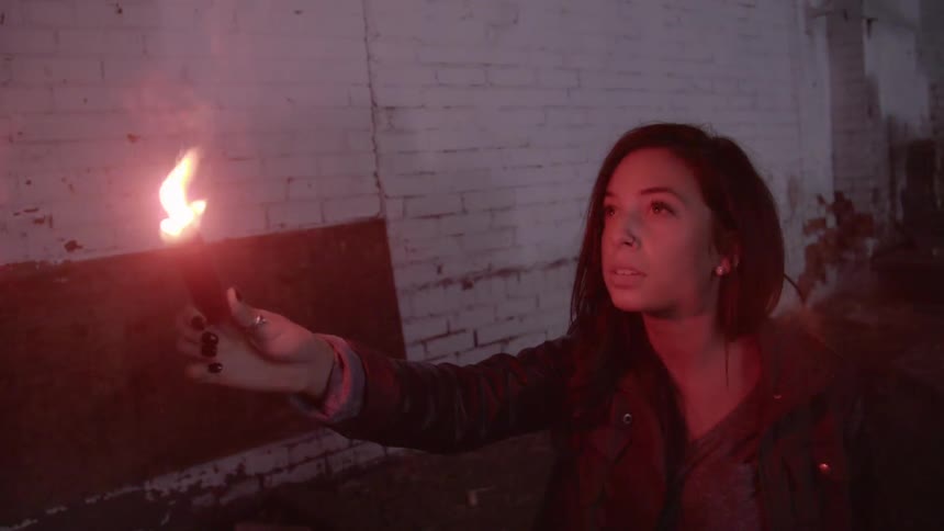 A woman holding a flare up next to a brick wall