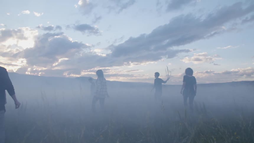 A group of young people walking into a foggy field at sunset