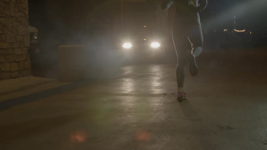 View of a woman's legs as she jogs past a car on an urban street