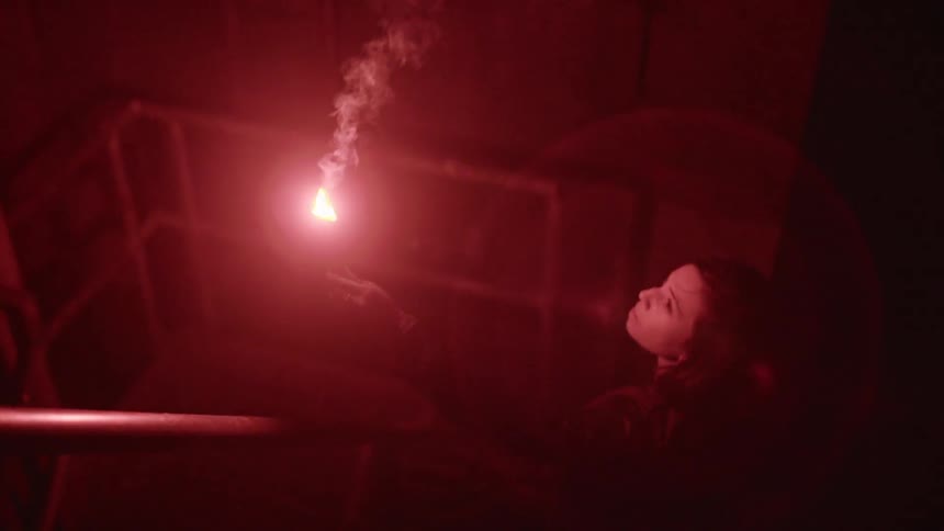 A woman uses a red flare to light a stairwell as she climbs up it and looks around