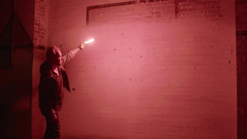 A man shines a red flare along a blank white brick wall