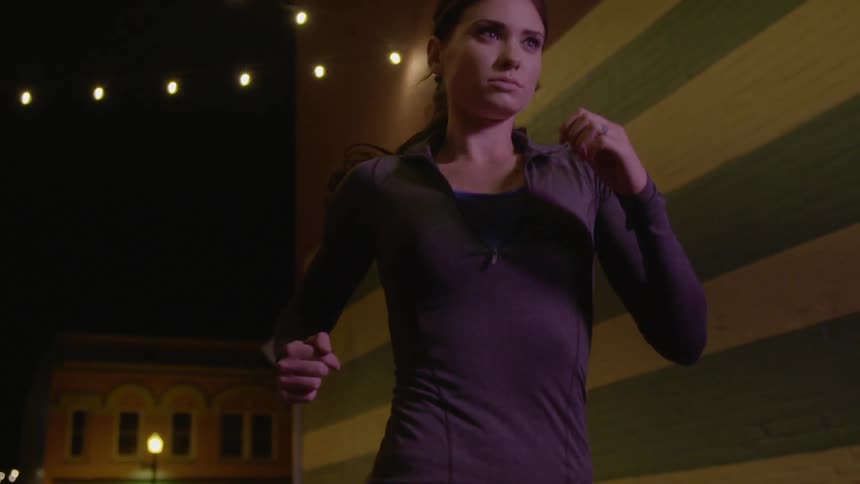 A young woman in athletic wear jogging in a town at night