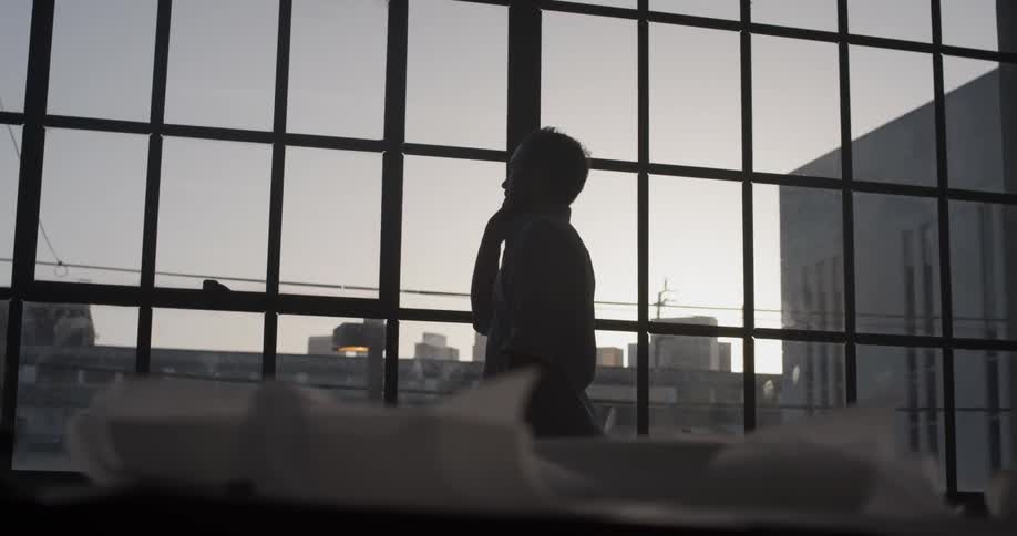 A man pacing around in front of a window talking on a phone