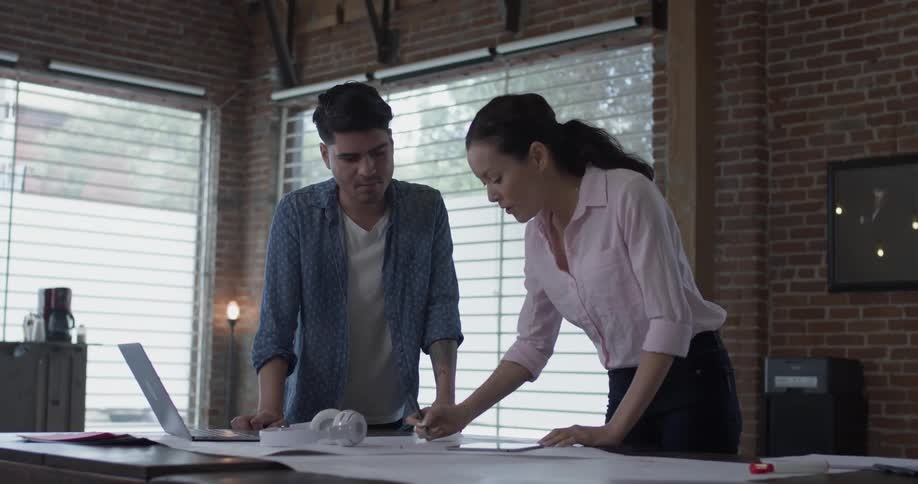 A woman makes notes on a large piece of paper after a man points something out on it