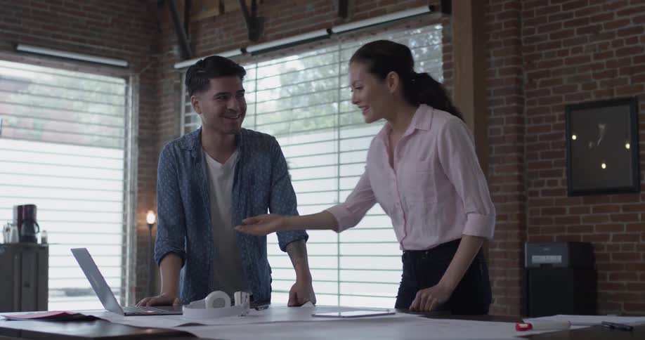 A man is describing something that he and a woman are looking at on a laptop on top of a desk in the office