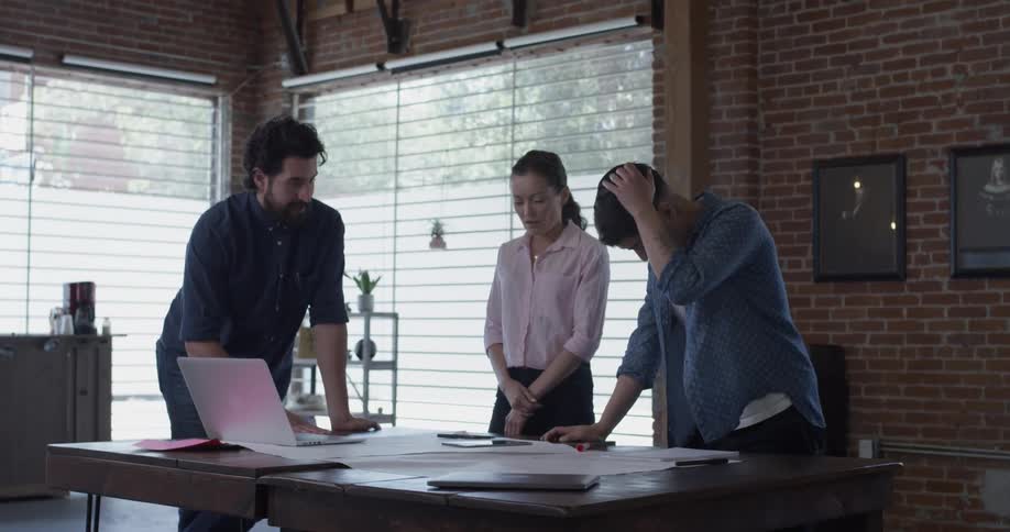 Three colleagues gather around a office table and discuss things with their hands on the table it looks serious on a bright sunny day