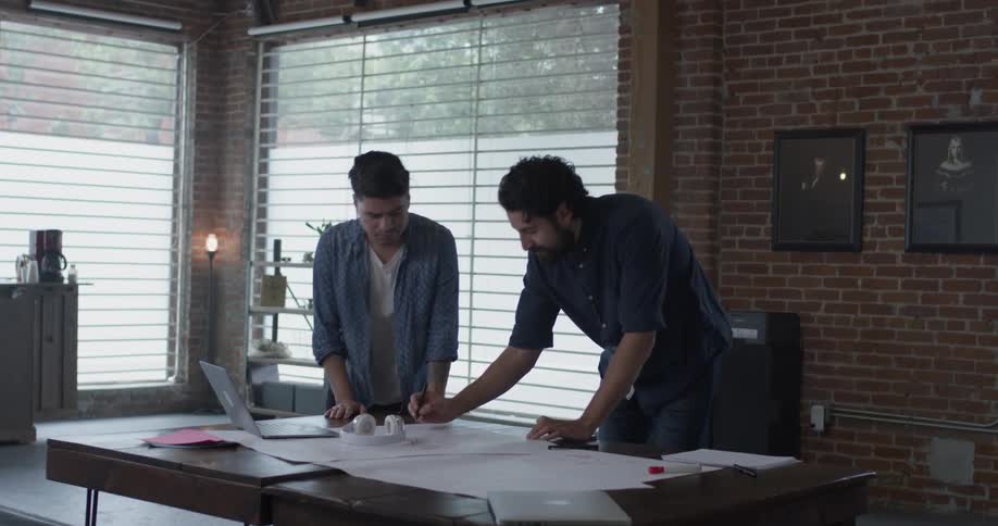 Two men standing around a desk talking about a design