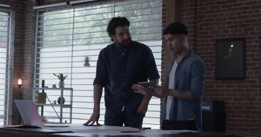 A man sketching on a piece of paper when another man walks in