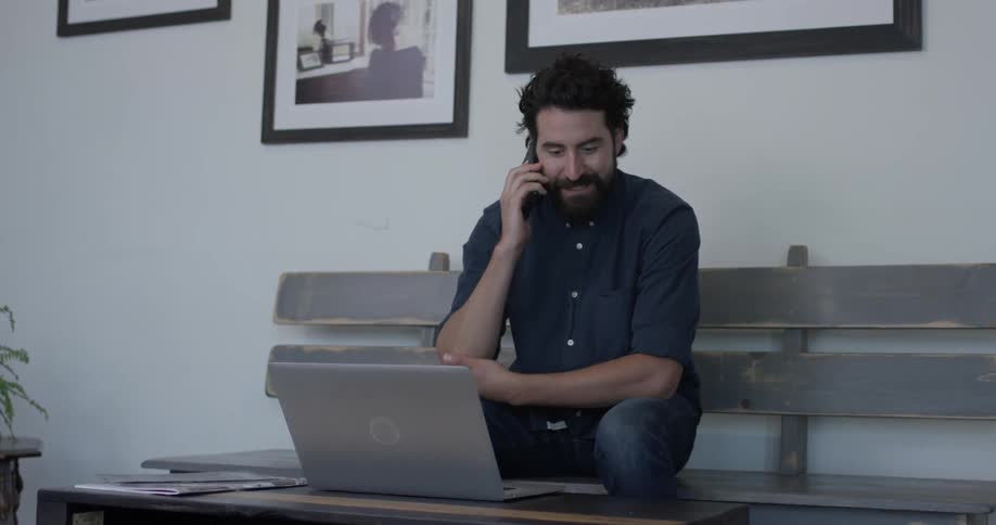A man is looking at a laptop and answering a phone