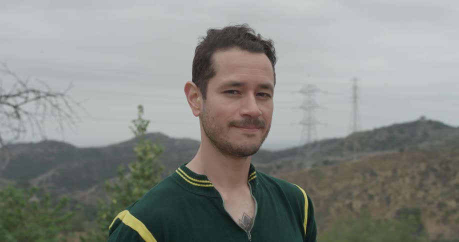 Smiling man stands outside near hills and power lines