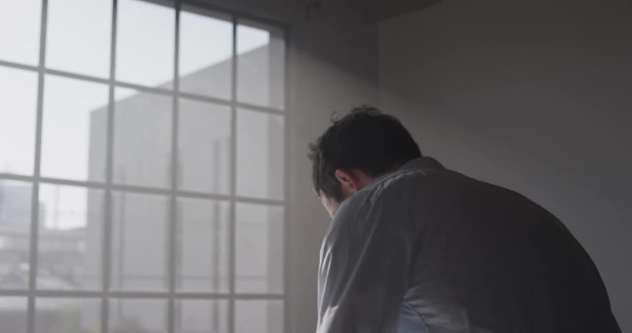 A man walks to a desk and leans over to write