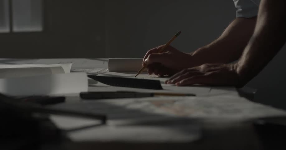 A man is sketching or drawing out some things on paper on a table