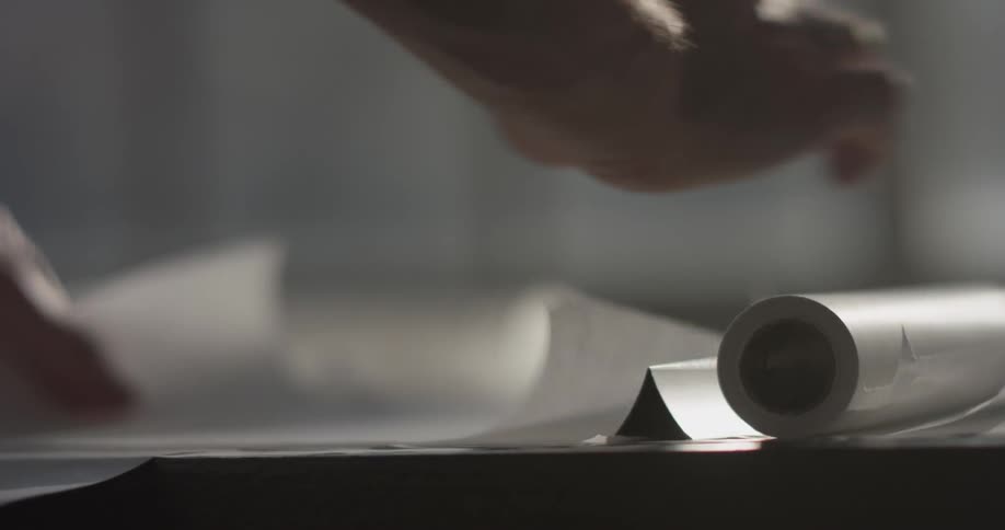 A man's hands move drawing papers around on a desk and draw with a pencil