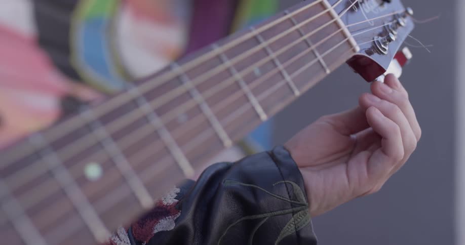 A woman tunes a guitar then starts to make a chord on the fretboard