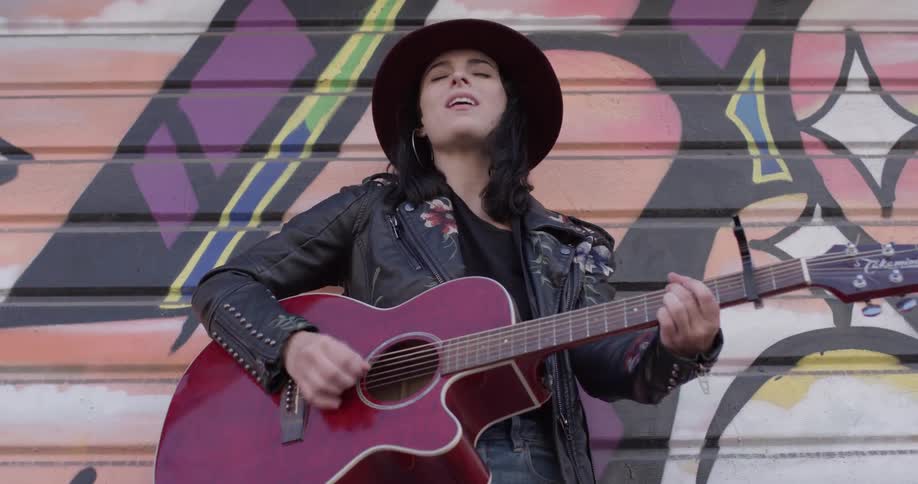 A woman strumming a guitar in front of a painting
