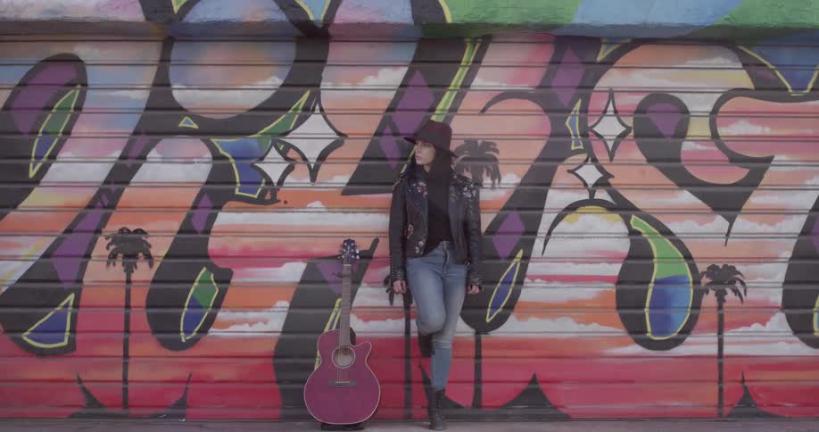 A woman standing next to a guitar in front of a mural