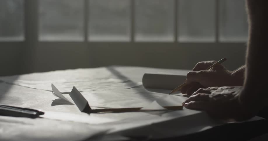 Man drawing on a large paper lined table in front of a window