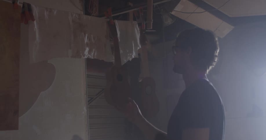 A man hanging up a guitar in a wood shop