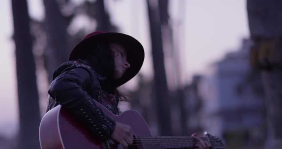 A woman sitting on a grassy hill playing guitar