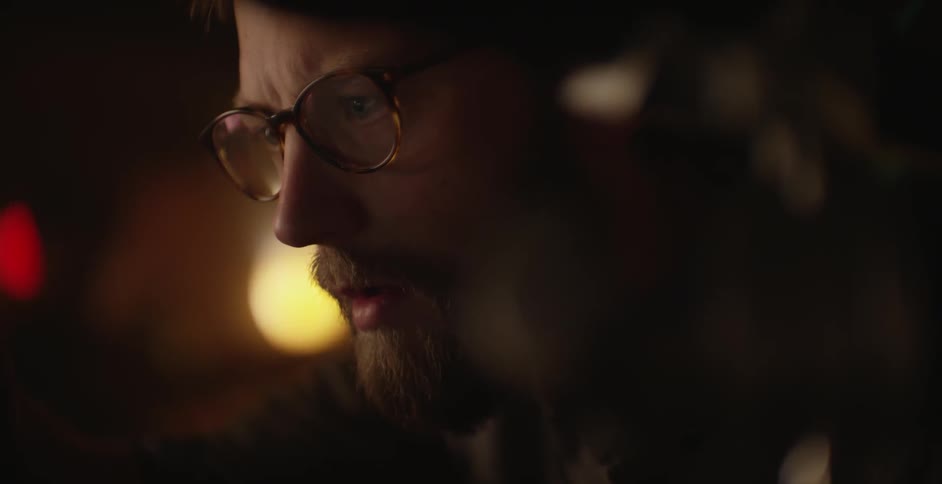 A brunette man, who wears glasses, leaning forward, gesturing and speaking before he types on a touchscreen