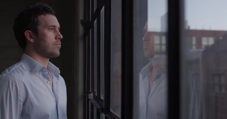 A man walks to the large windows and stares at the view
