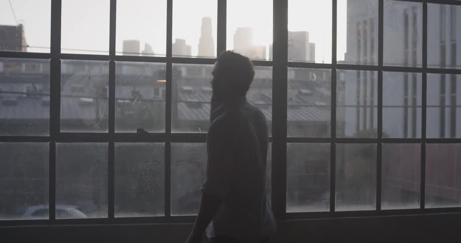 A man is talking on the phone while looking out the window at the skyline